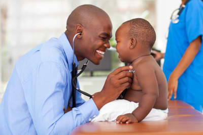 happy male doctor examining baby boy with female nurse on background